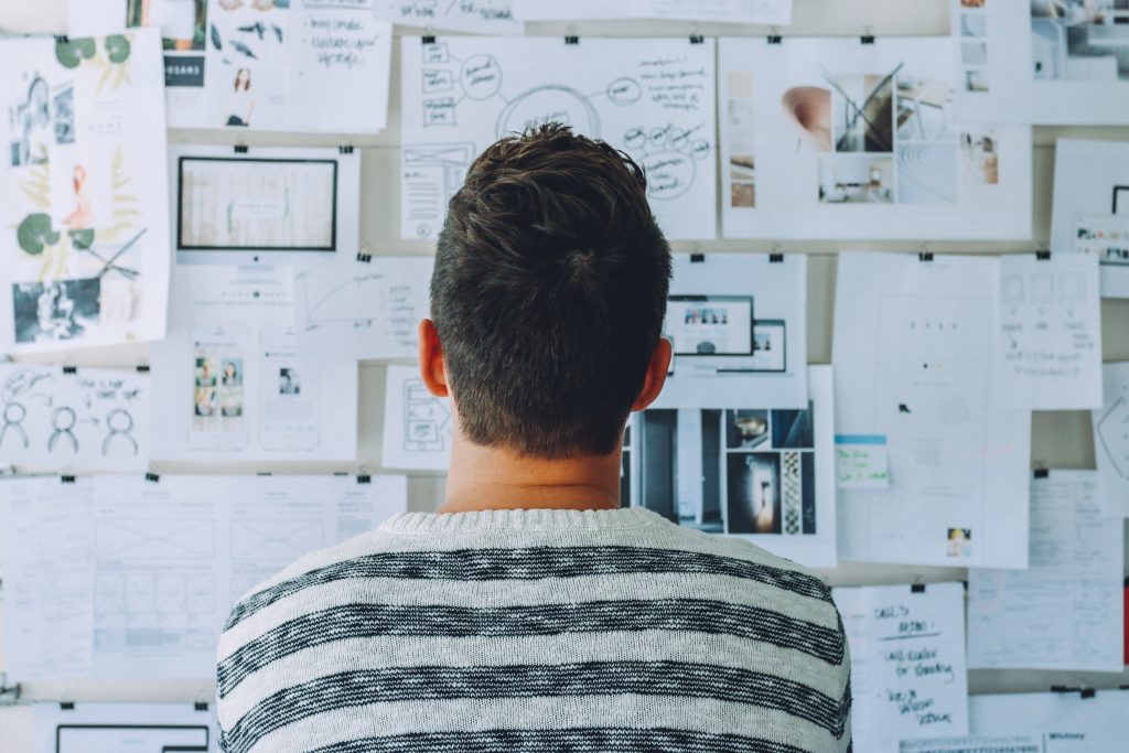 man standing in front of a wall filled with ideas and plans.