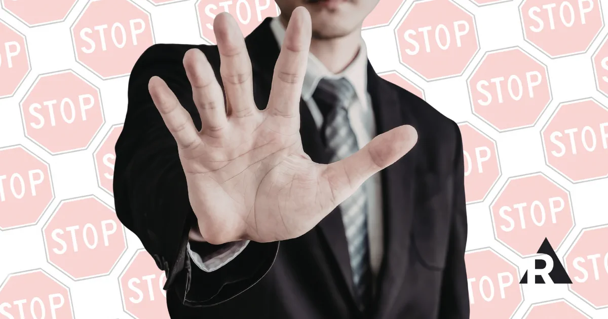 Person in a suit holding up a hand in a stop gesture against a background of stop signs